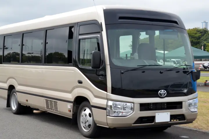 Beige and black mid-size minibus with tinted side windows parked on a paved lot, in front three-quarter view.