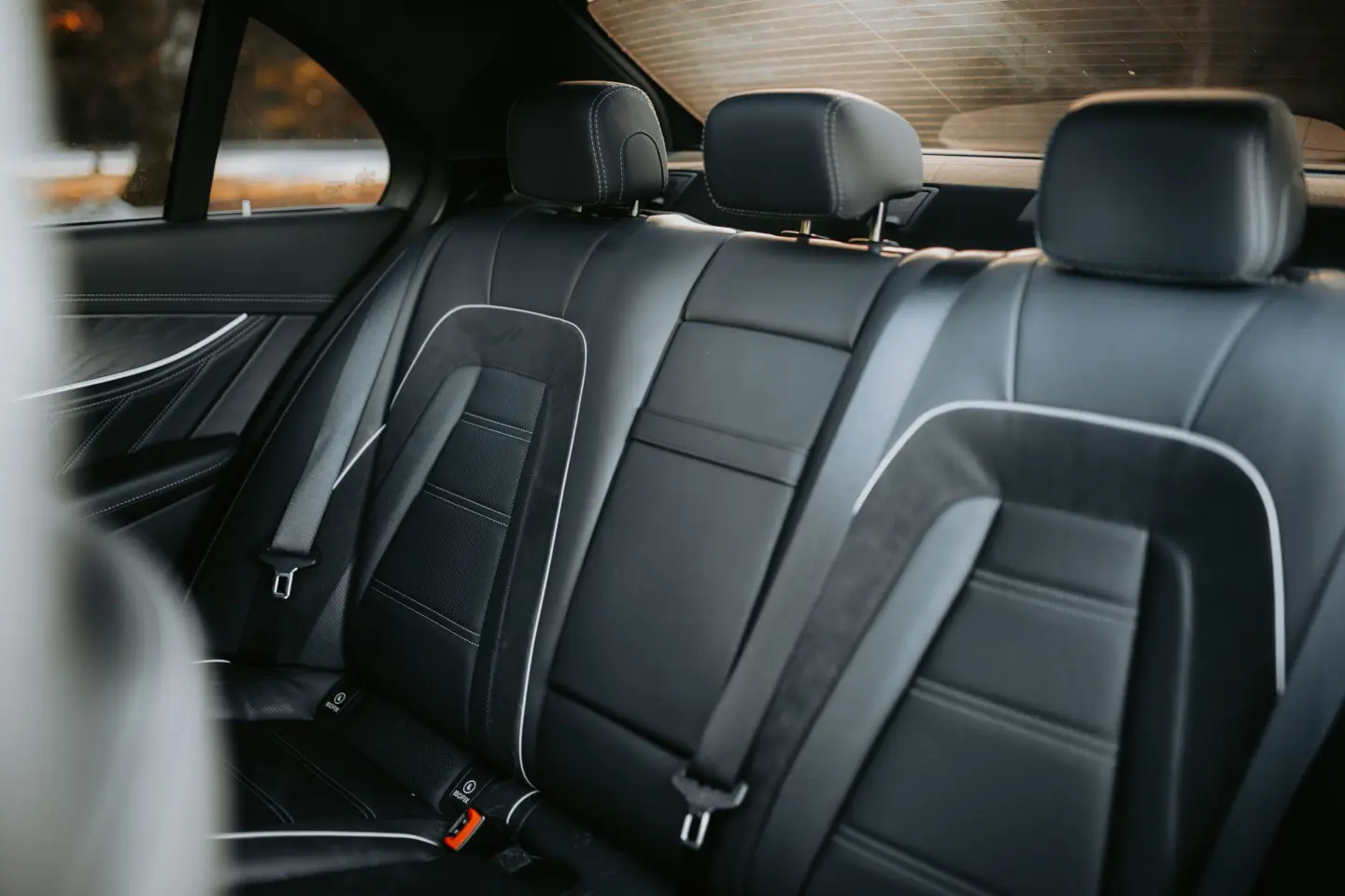 Black leather rear bench seat of a luxury sedan with white piping, suede inserts and three headrests.