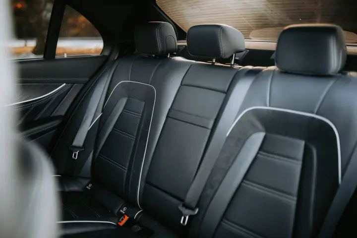 Black leather rear bench seat of a luxury sedan with white piping, suede inserts and three headrests.