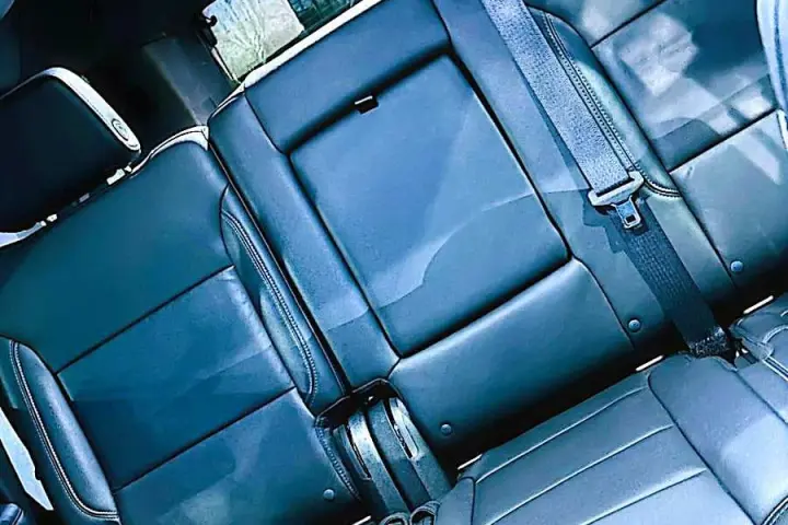 Black leather rear bench seat with seat belts inside a full-size SUV, seen past the center console.