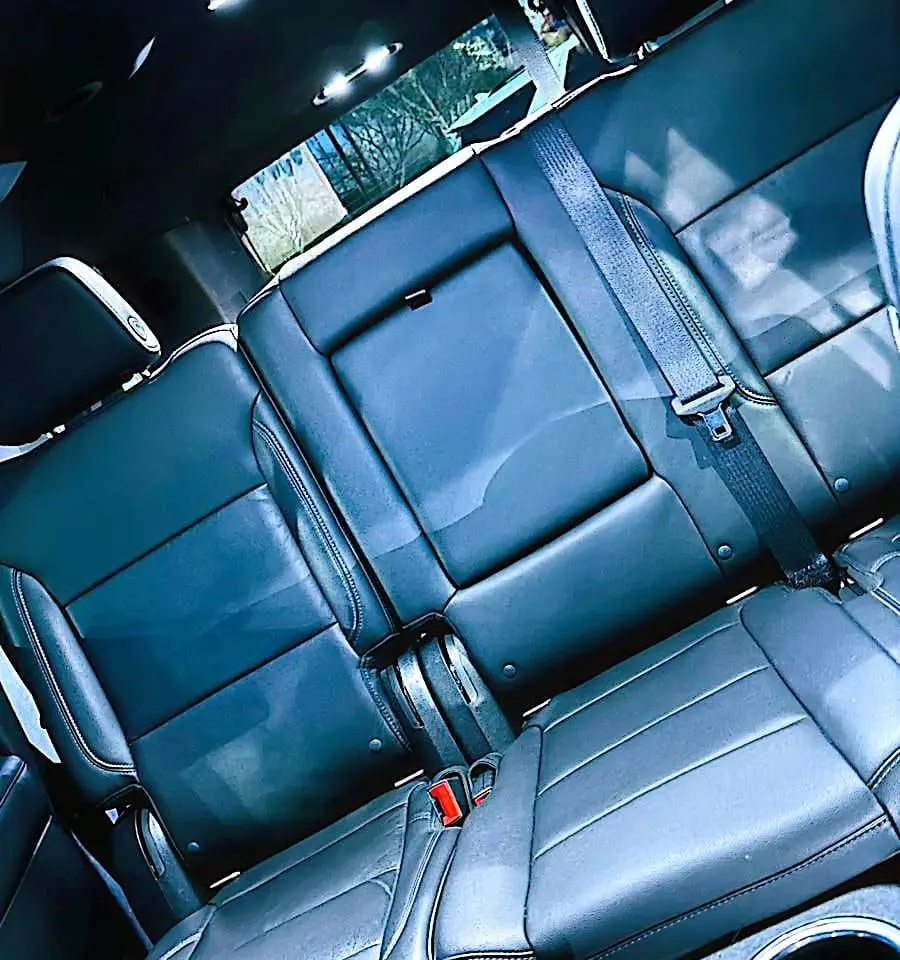 Black leather rear bench seat with seat belts inside a full-size SUV, seen past the center console.
