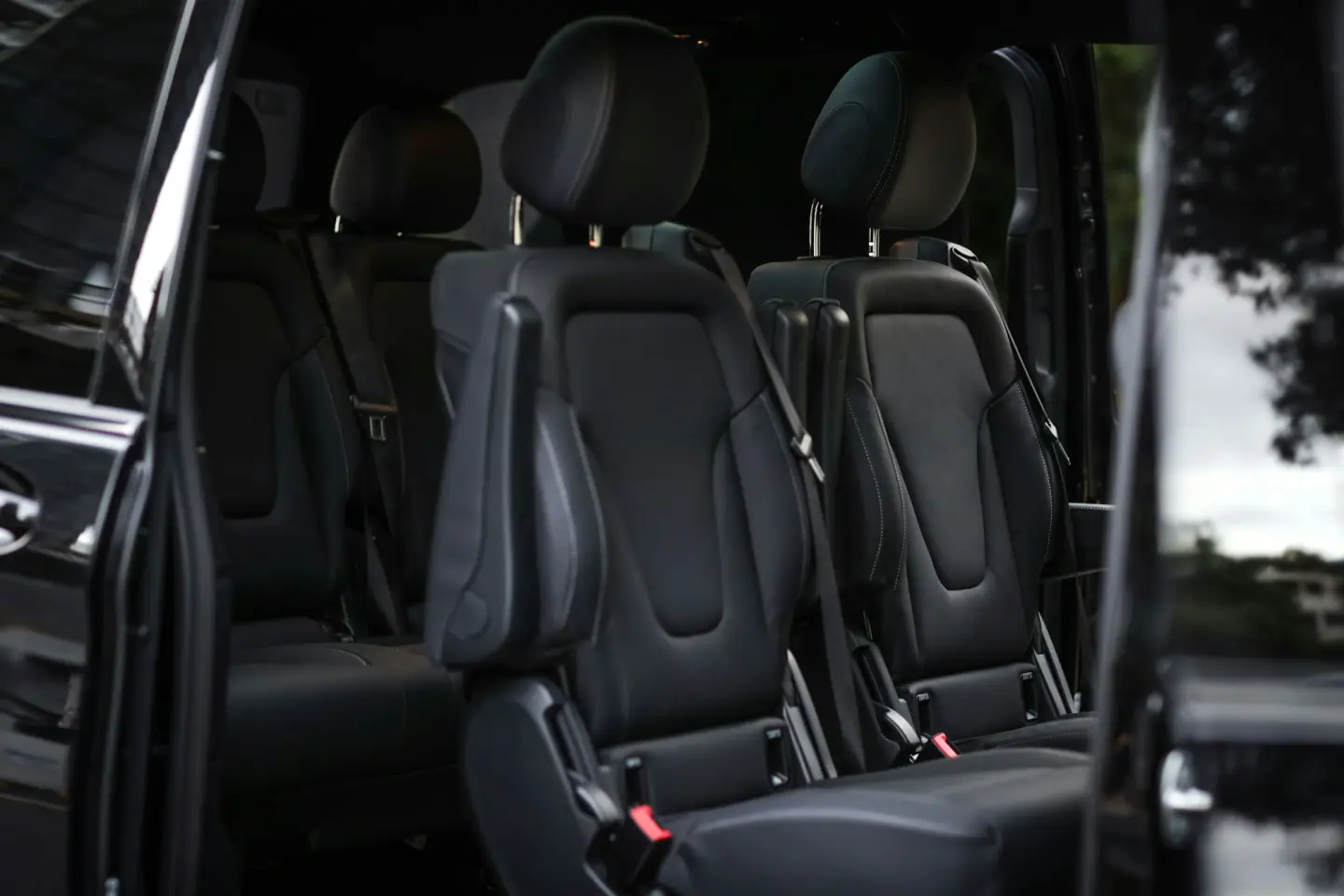 Black leather captain seats with seat belts inside a passenger van, seen through the open side door.
