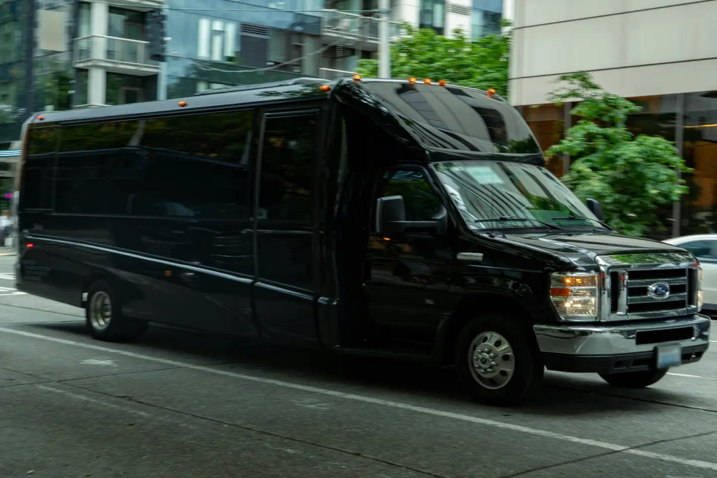 Black mid-size limo bus with tinted windows and amber roof lights driving down a city street.