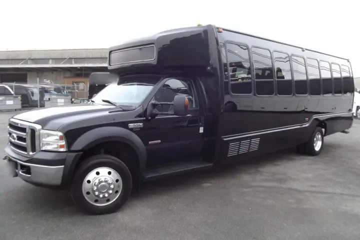 Black limo party bus with tinted windows and chrome wheels, parked in a lot in front three-quarter view.