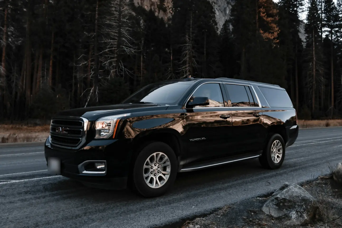 Black GMC Yukon XL full-size SUV parked on a mountain road bordered by tall pine trees.