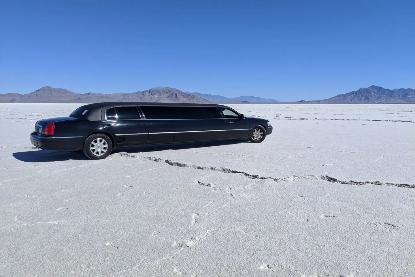 Black Lincoln Town Car stretch limousine parked on a white salt flat under a clear blue sky, with mountains behind.