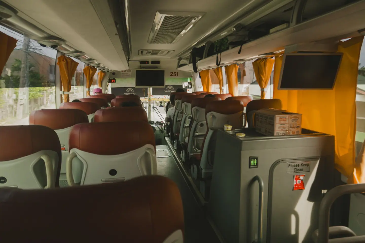 Charter coach cabin with red and white high-back seats, overhead TV screens and yellow curtains along the aisle.