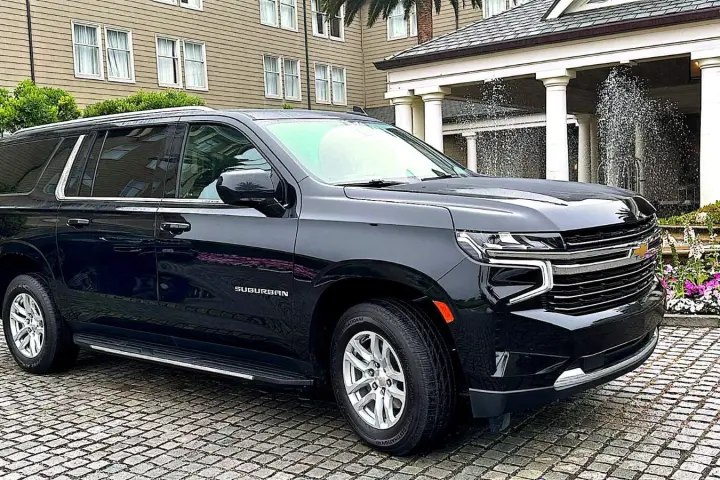 Black Chevrolet Suburban SUV parked on a cobblestone hotel forecourt beside a fountain and flower beds.
