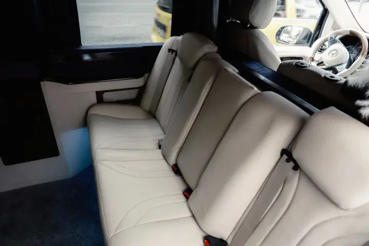 Cream leather rear bench seats with seat belts inside a luxury vehicle, with the driver cab visible ahead.