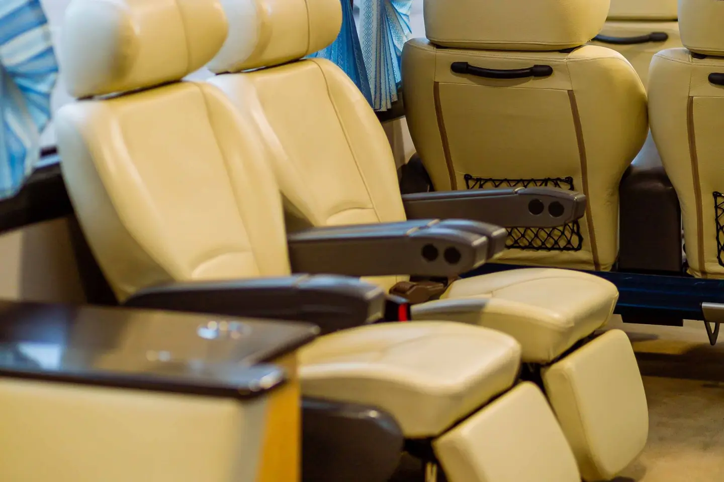 Cream leather reclining seats with armrests and fold-out leg rests inside a passenger bus.