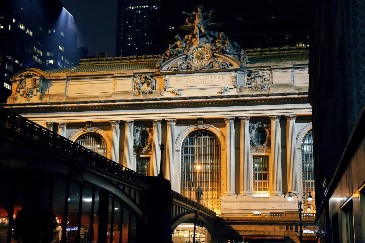 Floodlit facade of Grand Central Terminal at night, with its clock and sculpture group above the arched windows.