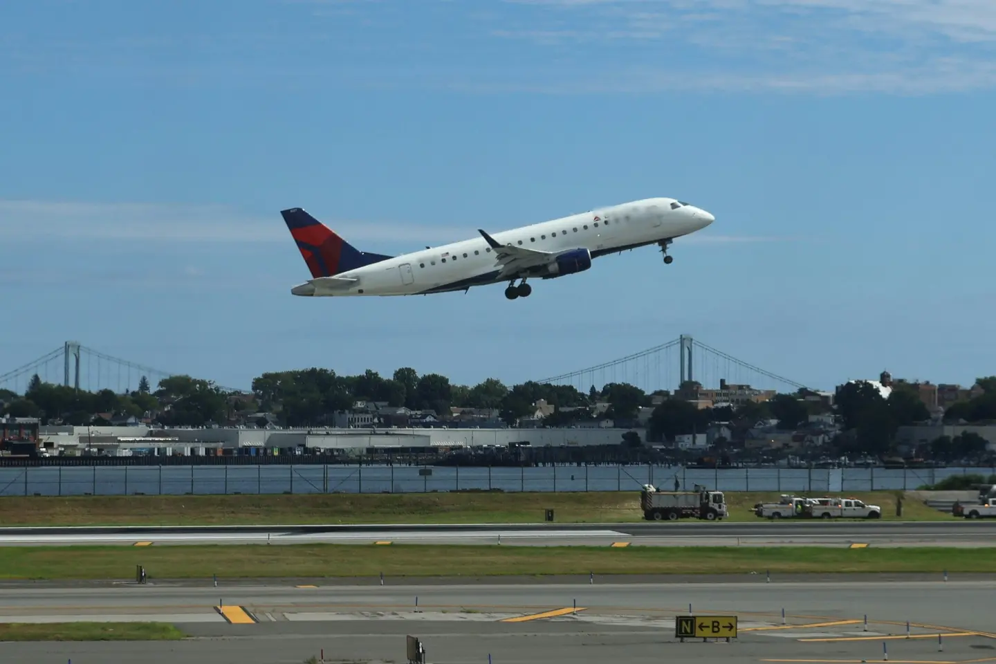 Regional passenger jet lifting off from a LaGuardia Airport runway, with suspension bridges across the water behind.