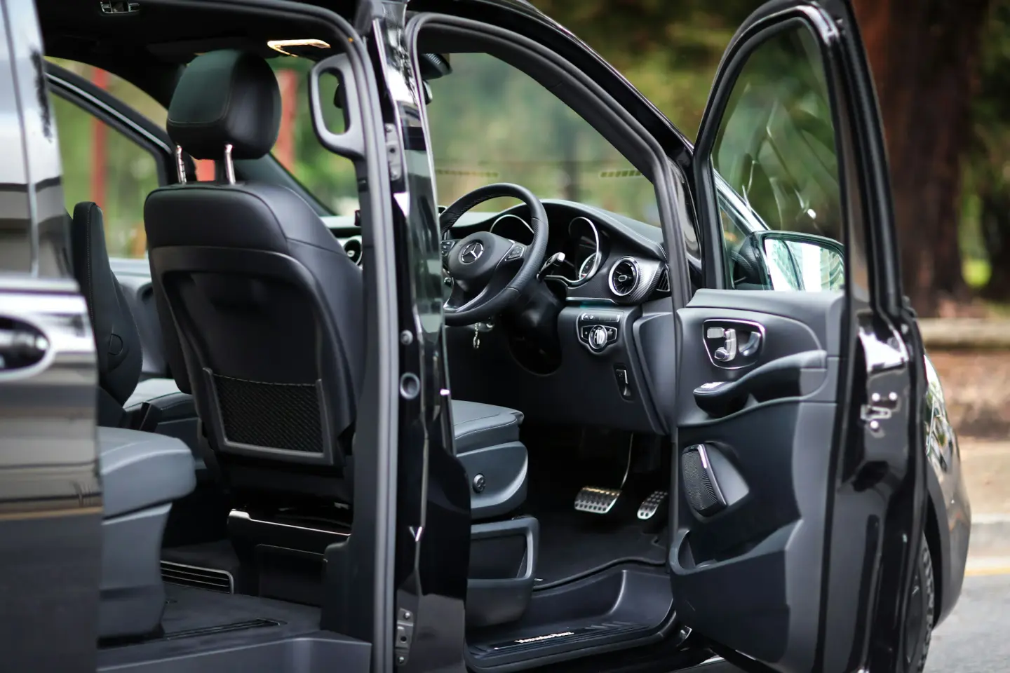 Open front and side doors of a black luxury van, showing black leather seats, the dashboard and the steering wheel.