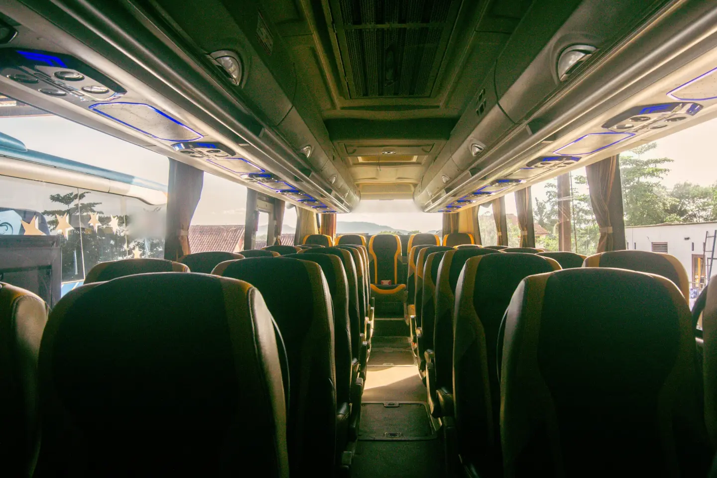 Empty motorcoach cabin viewed down the aisle, with high-back seats and luggage racks with blue lighting.