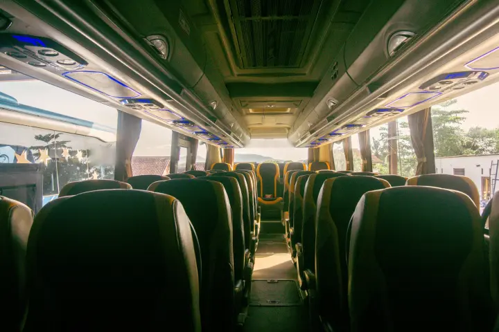 Empty motorcoach cabin viewed down the aisle, with high-back seats and luggage racks with blue lighting.