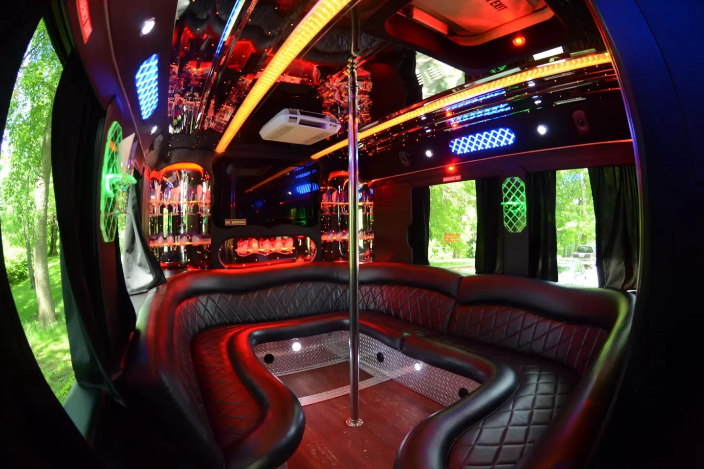 Party bus interior with black diamond-stitched wraparound seating, a chrome pole, LED lighting and a mirrored bar.