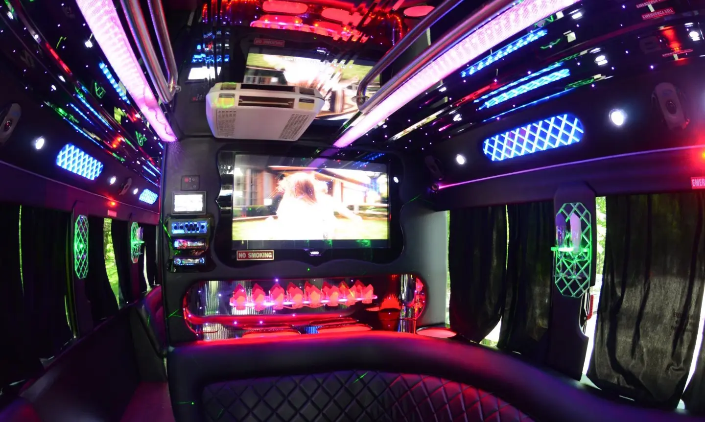 Party bus lounge with black diamond-stitched leather seating, a red-lit bar, a TV and purple, blue and green LED lights.