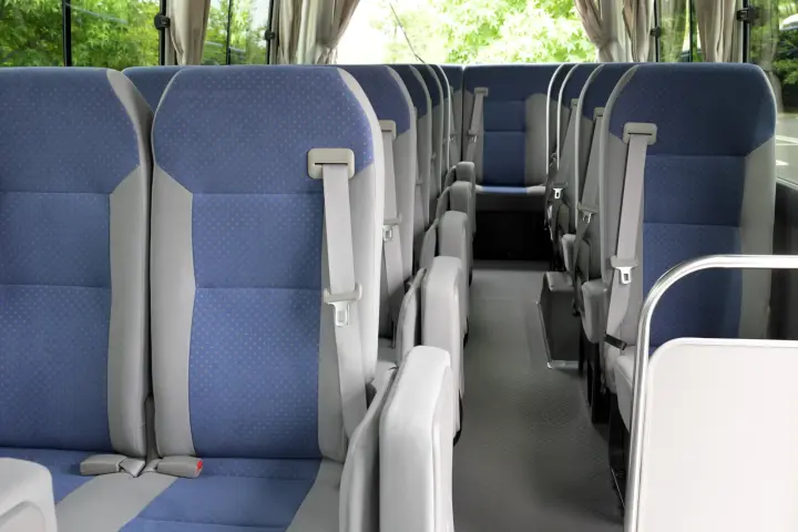 Minibus aisle view with blue and gray fabric seats, seat belts, fold-down aisle seats and cream curtains.