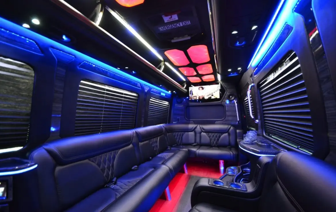 Sprinter limo cabin with black leather lounge seating, blue accent lighting, window blinds and a red-lit floor.