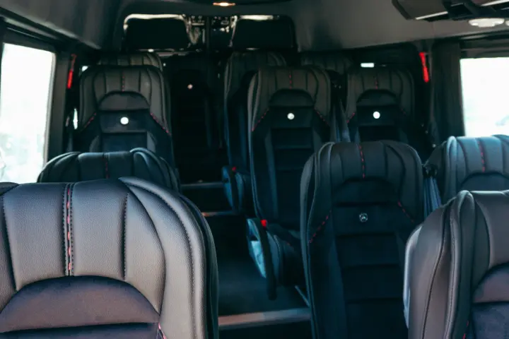 Aisle view of a Sprinter van cabin with rows of black leather and suede passenger seats with red stitching.
