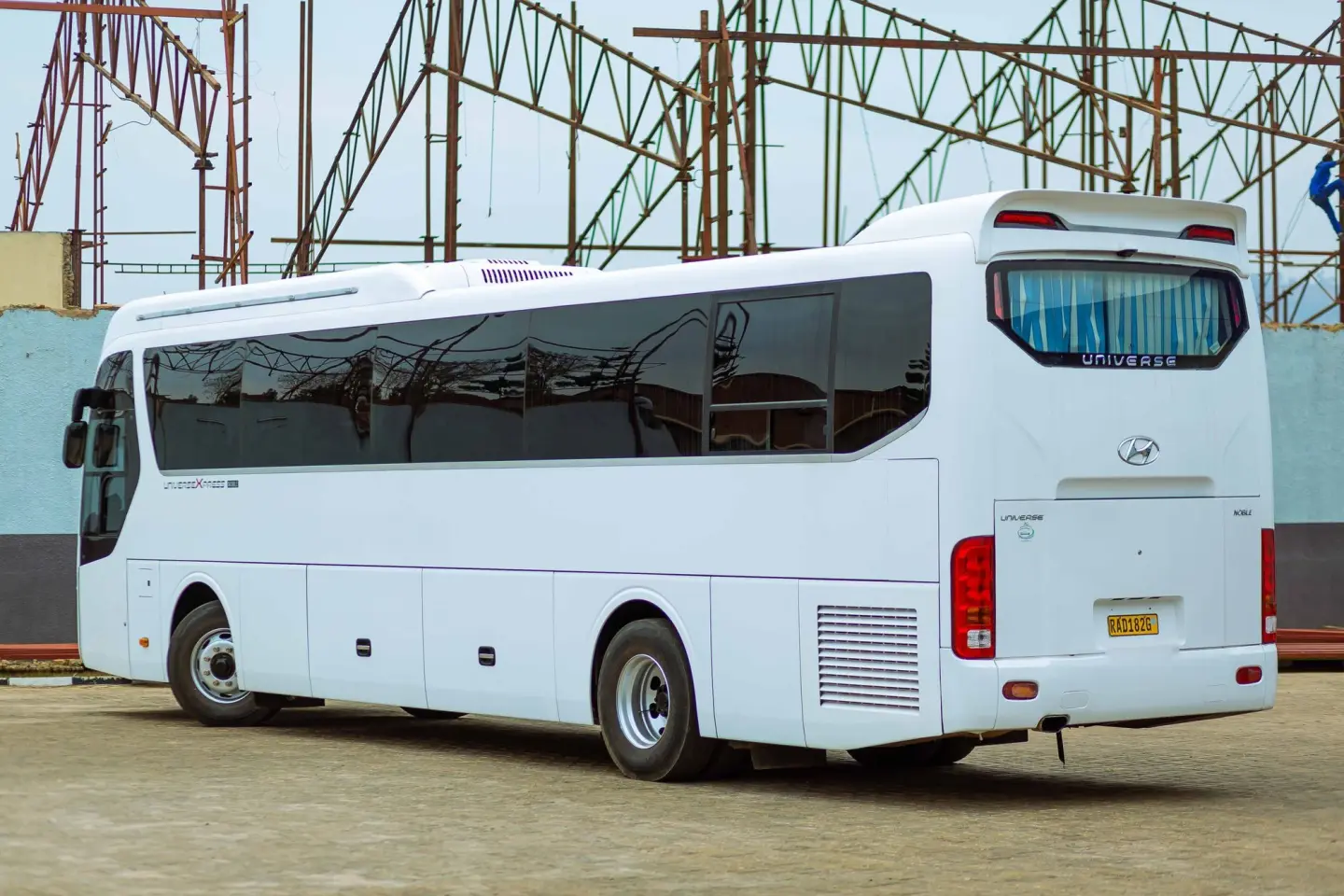 White Hyundai Universe coach bus with tinted windows parked in an open lot, seen from the rear three-quarter.