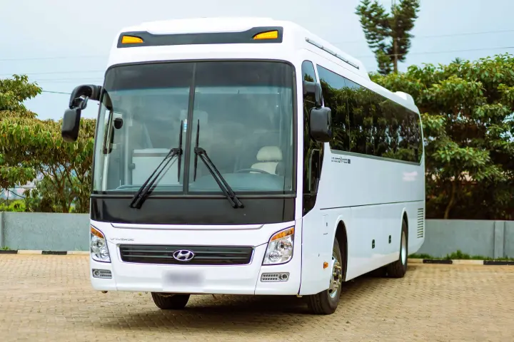 White coach bus with dark tinted windows parked on a brick-paved lot in front three-quarter view, with trees behind.