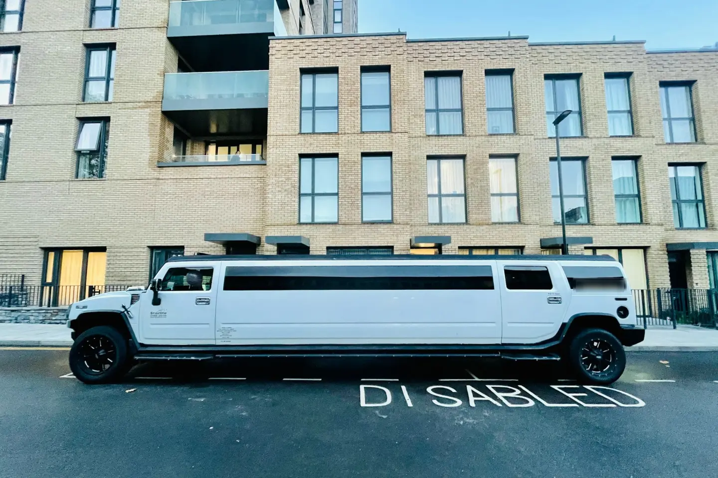 White Hummer H2 stretch limousine with black wheels parked at a city curb in front of a brick apartment building.